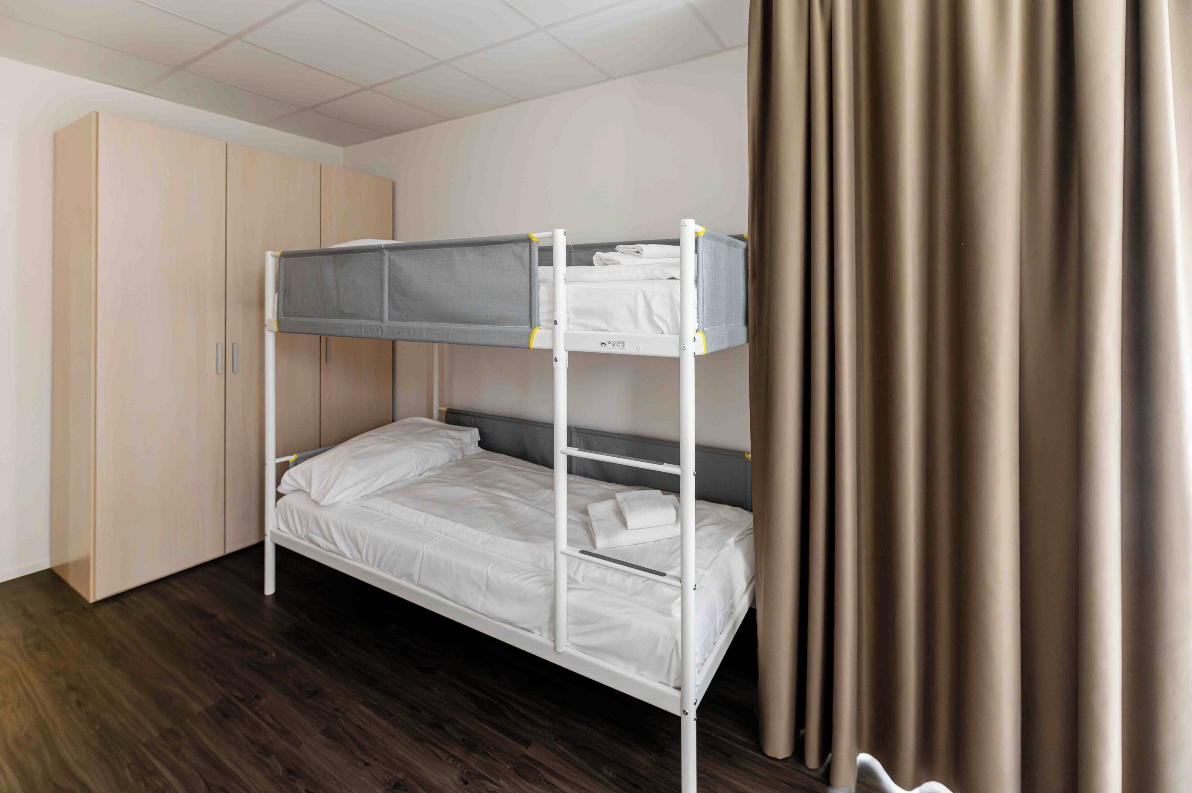 A bunk bed with a desk attached, a wardrobe, and a curtain.