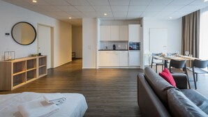 A modern hotel room with a bed, a sofa, a dining area, and a kitchen.