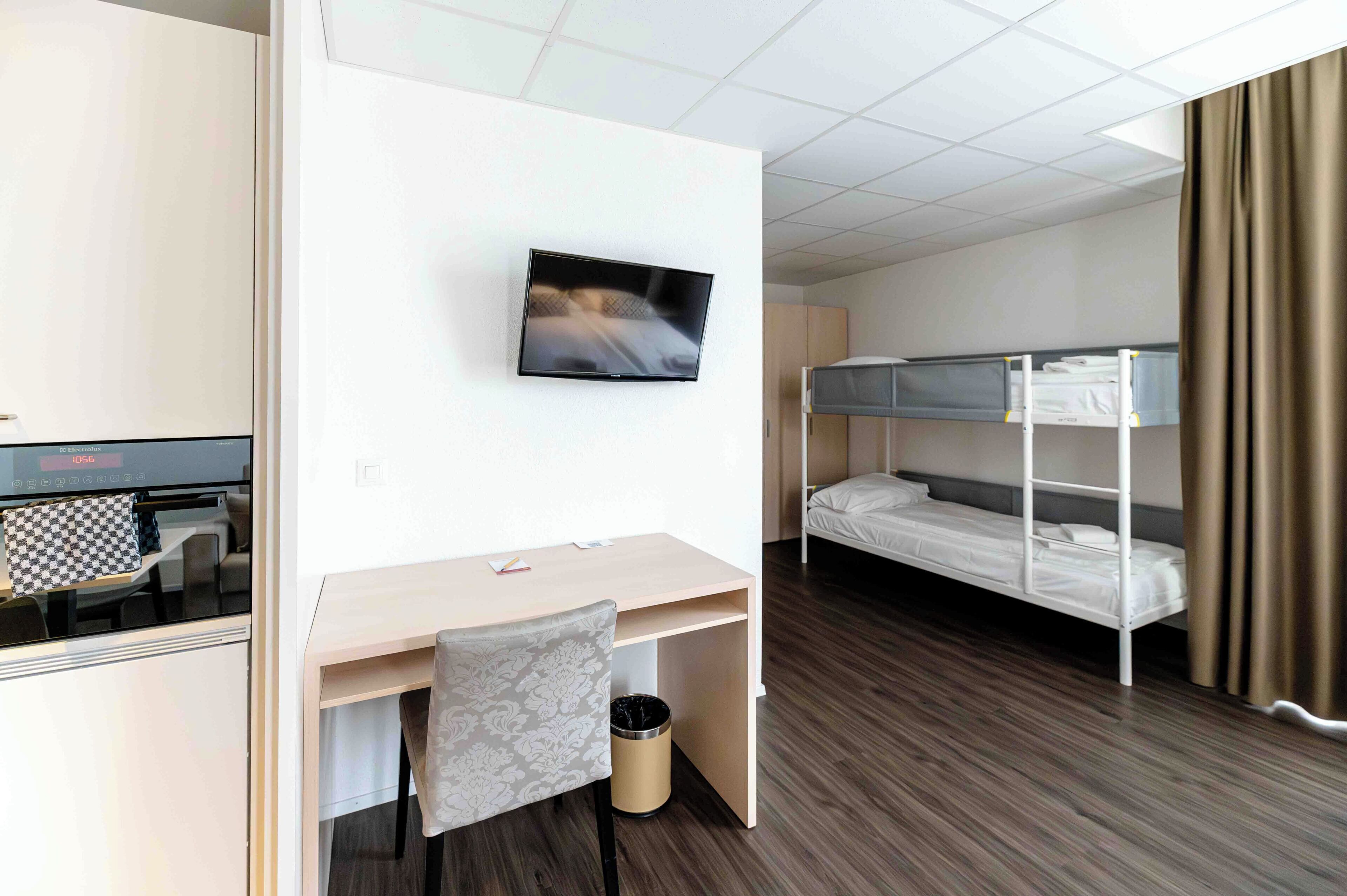 Une chambre d’hôtel équipée d’un lit, d’un bureau, d’une chaise, d’une télévision et d’un lit superposé.