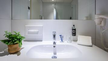 Un baño moderno con un lavabo blanco, una planta en maceta, una toalla y un secador de pelo.