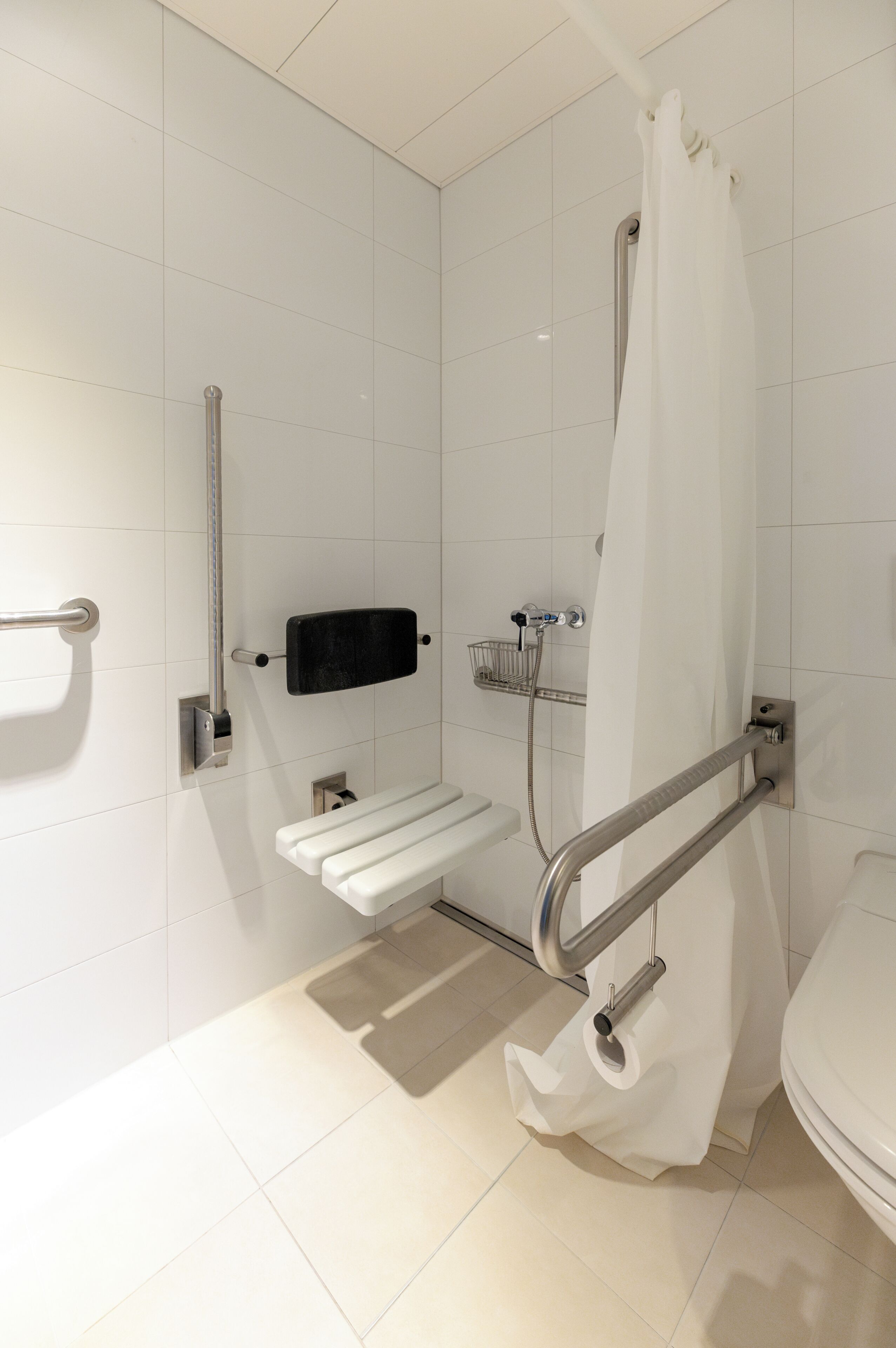 A modern bathroom with white tiles, a shower with a curtain, a grab bar, a towel rack, and a toilet.