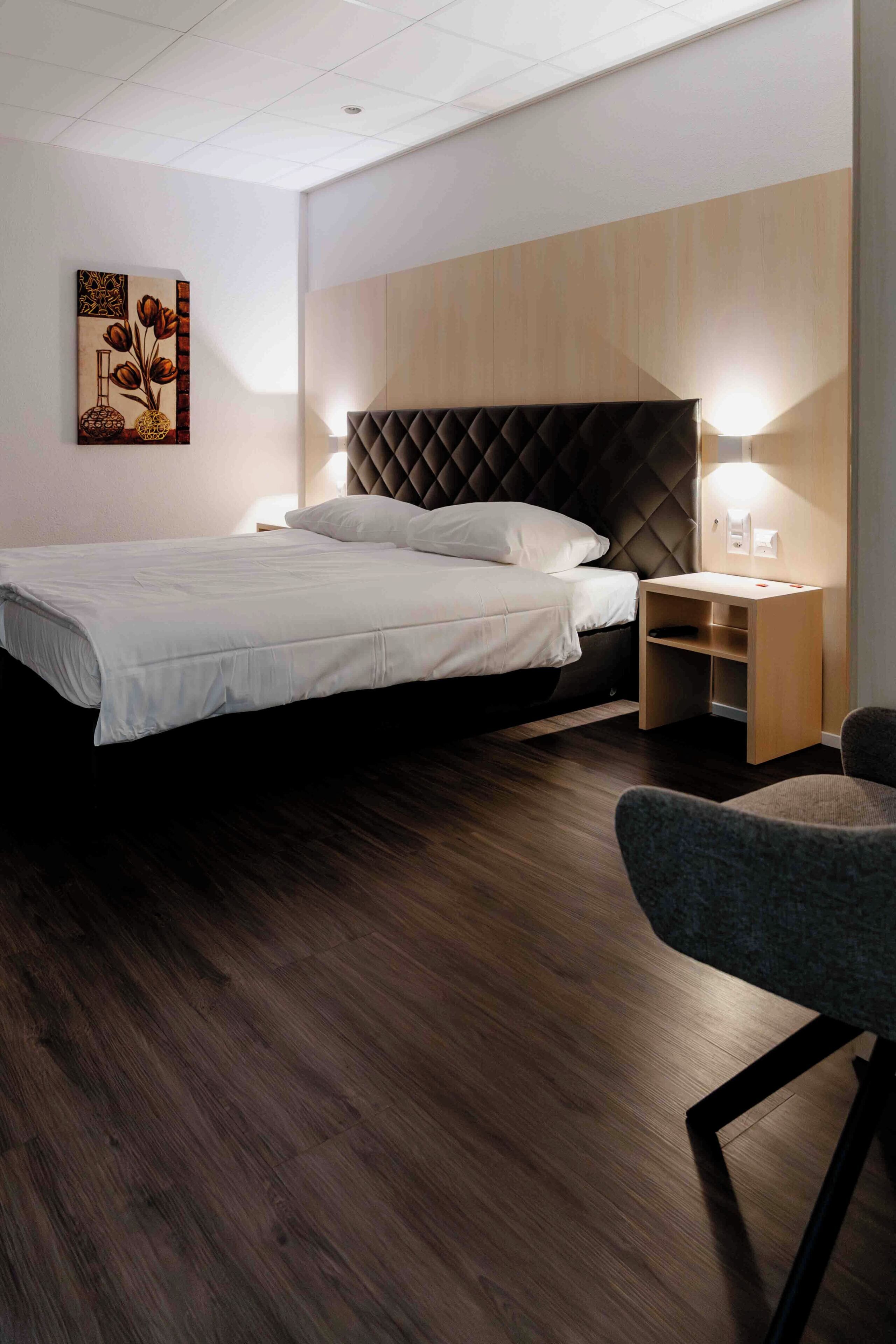 Une chambre moderne avec un grand lit, des tables de chevet, une chaise et un luminaire fixé au mur.