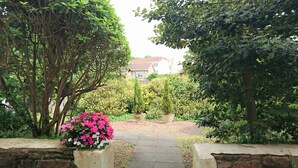 Un sendero en un jardín que lleva a una casa, rodeada de follaje y plantas con flores.