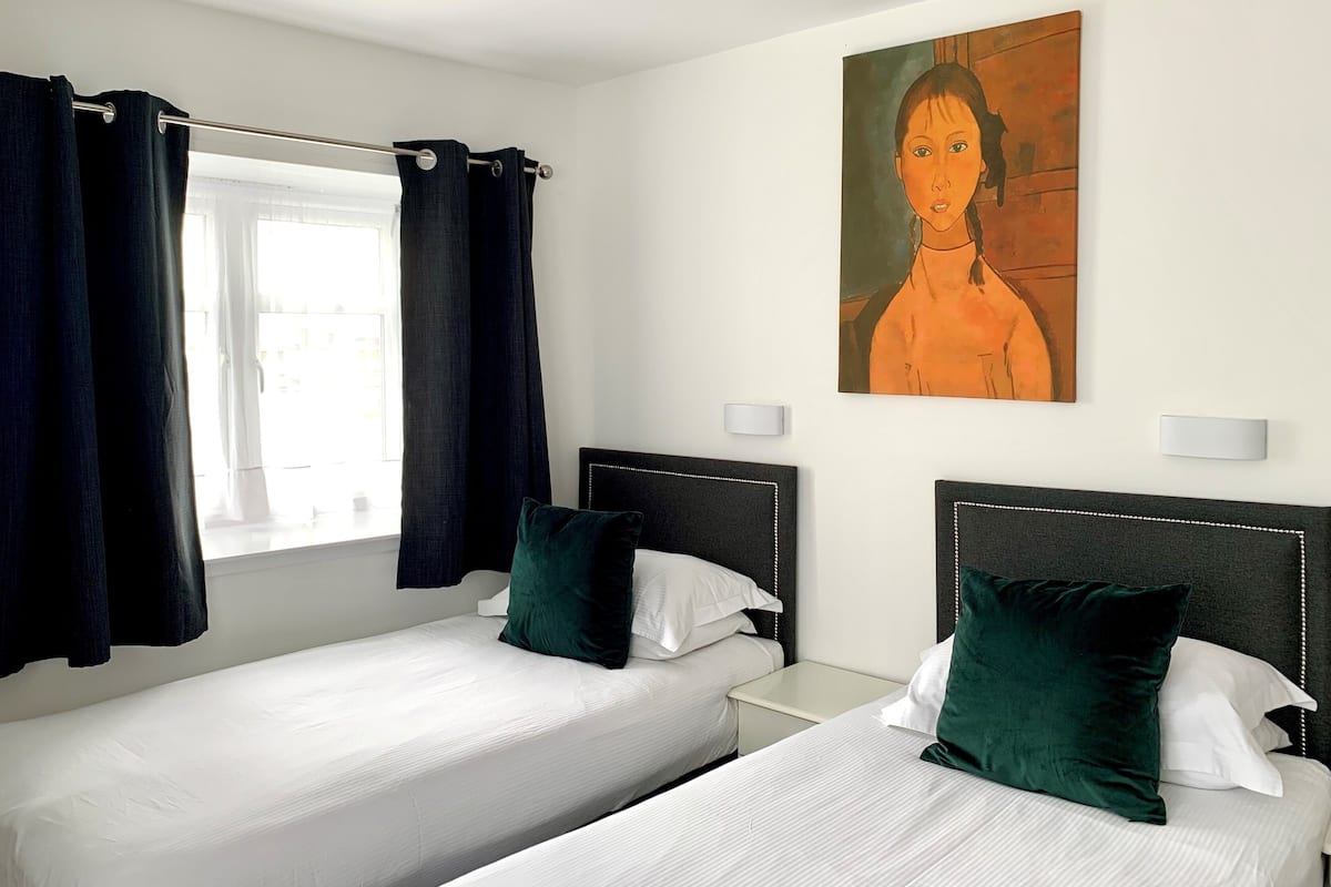 Habitación de hotel con dos camas individuales, cortinas oscuras, un cuadro en la pared y lámparas de noche.