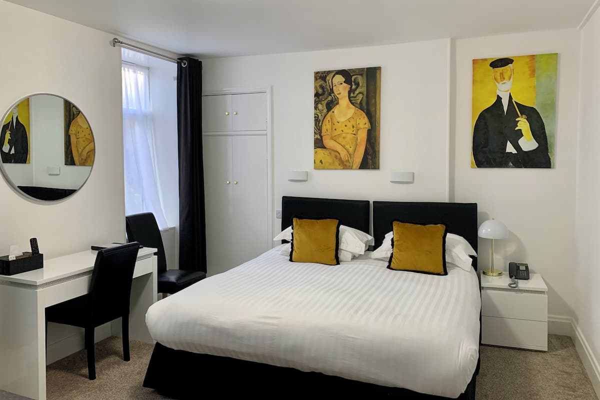 Una habitación de hotel con cama, escritorio, silla, armario y cuadros en las paredes.