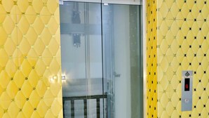 Porta de elevador de vidro com parede amarela estampada.
