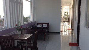 Um corredor limpo e bem iluminado, com um balcão de recepção, uma área de estar com duas cadeiras e uma mesa, e uma janela grande que oferece luz natural.