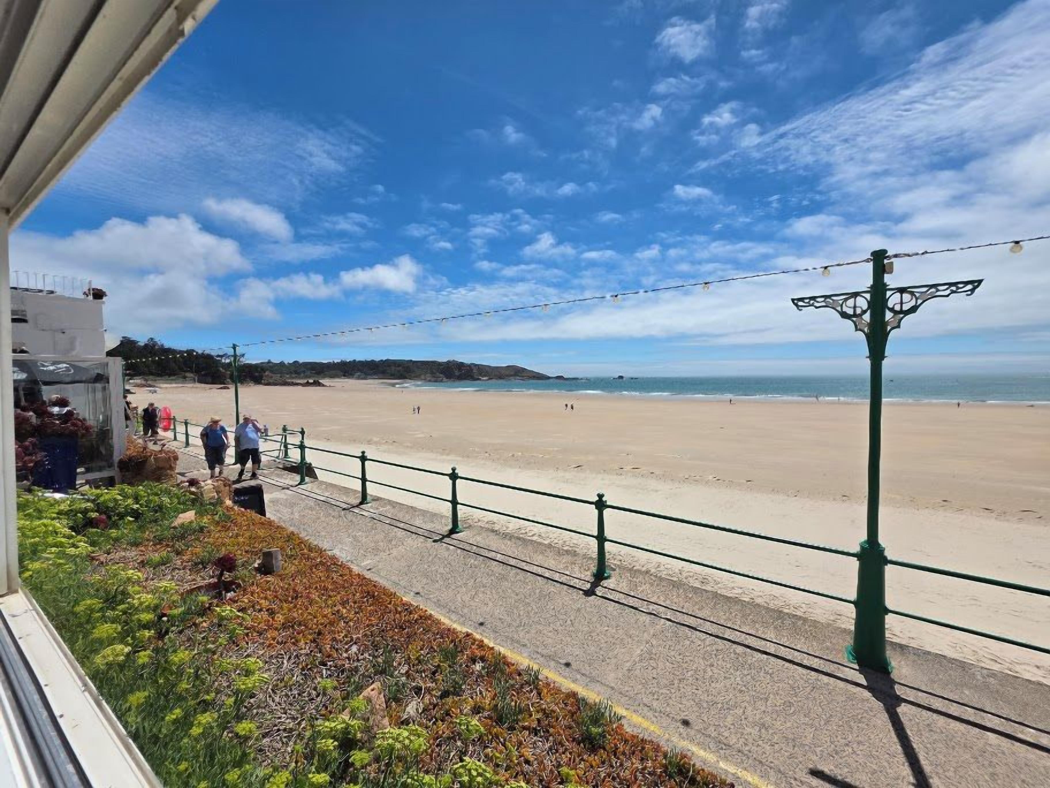 A coastal walkway with a view of the beach, a railing, and a street lamp.