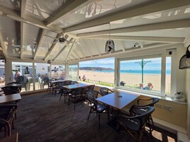 Un área de estar interior con mesas y sillas, grandes ventanales que ofrecen vista a la playa.