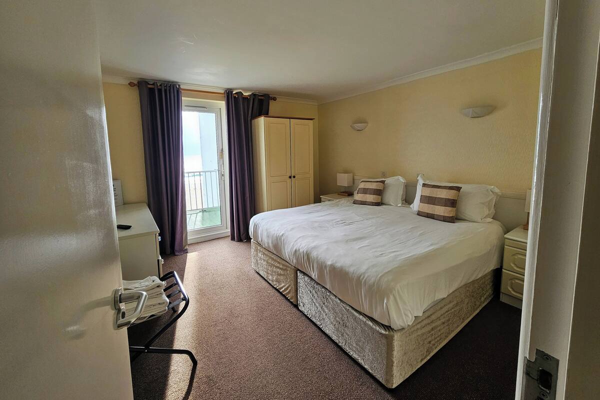A hotel room with a large bed, a desk, a chair, a wardrobe, and a balcony with curtains.