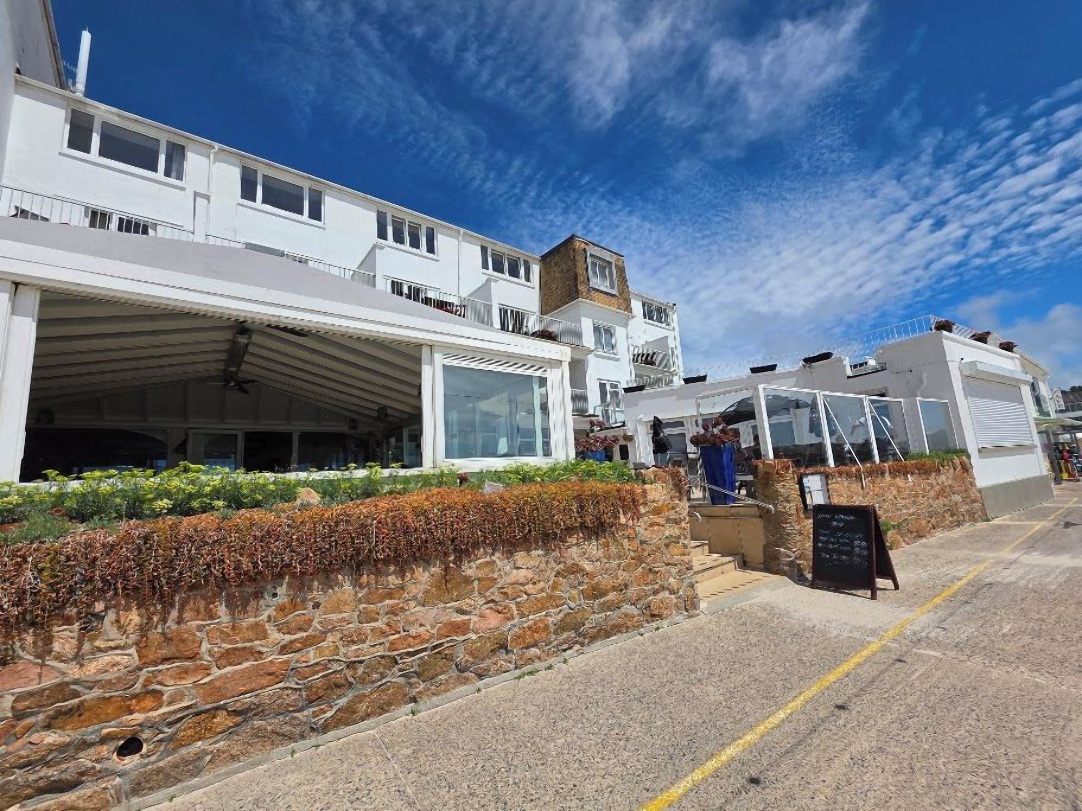 A coastal building with a stone facade, a covered outdoor seating area, and a clear sky.