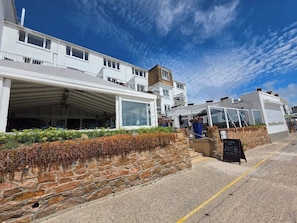 A coastal building with a stone facade, a covered outdoor seating area, and a clear sky. - The Beau Rivage (St. Brelade)