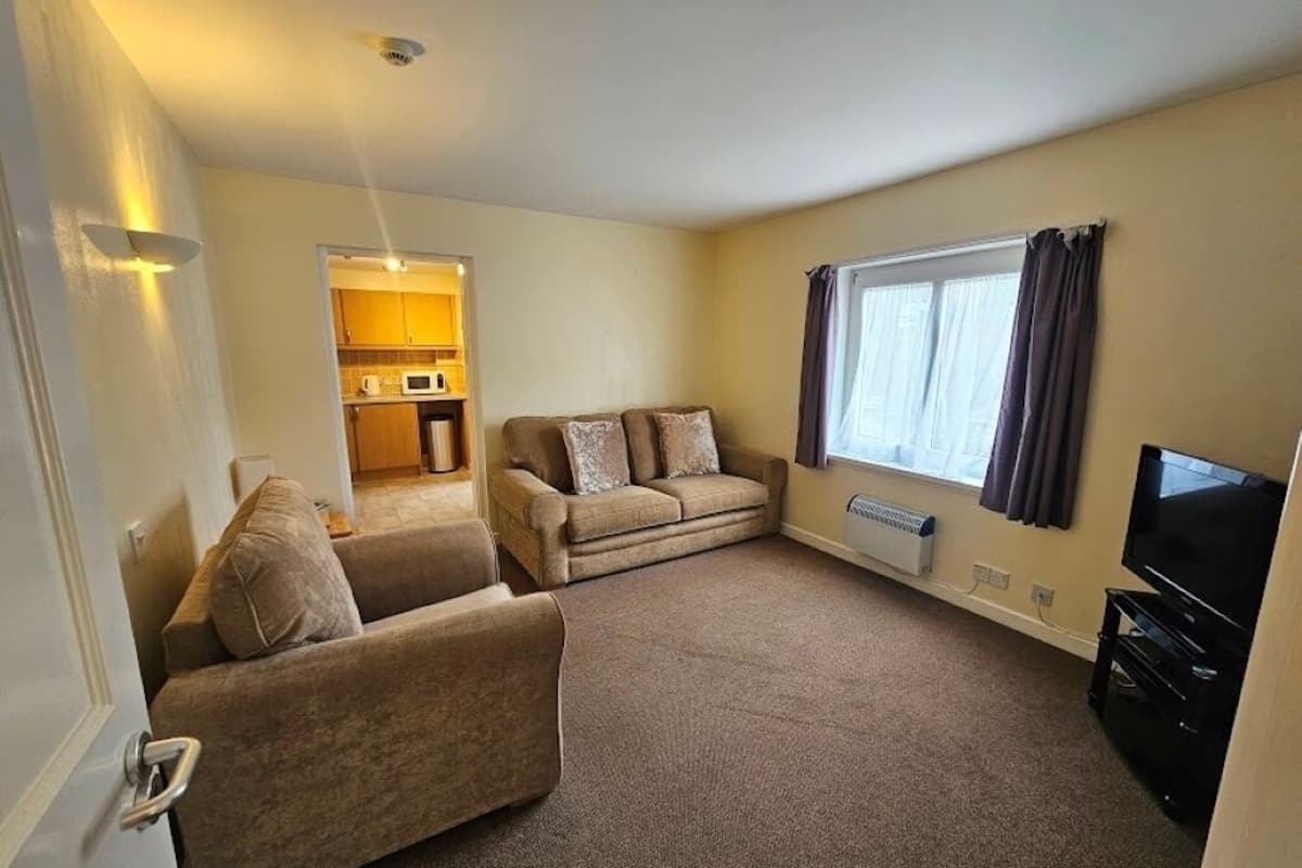 A living room with a sofa, a television, and a window with curtains.