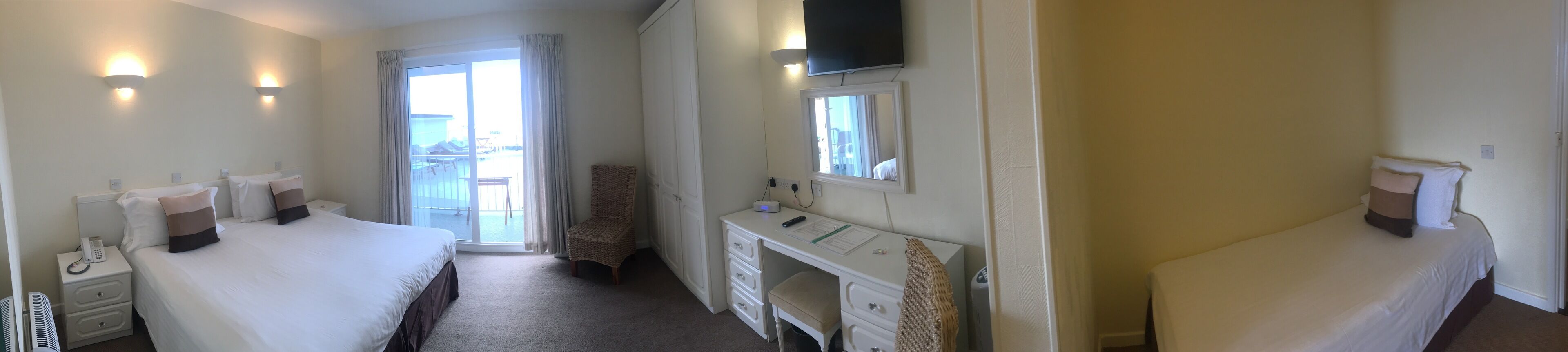 A hotel room with two beds, a desk with a flat-screen TV, a fireplace, and a balcony with curtains.