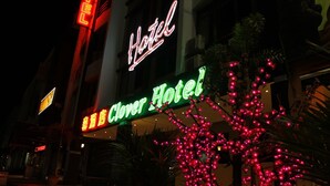 A hotel sign with neon lights, a neon sign for a hotel, and a tree with pink lights. - Clover Hotel (Masai)