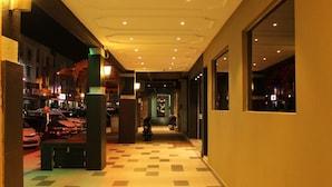 A hotel corridor with a checkered floor, recessed lighting, and large windows on one side. - Clover Hotel (Masai)