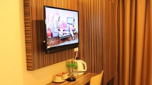 A hotel room with a wooden desk, a television mounted on the wall, a chair, and a curtain. - Clover Hotel (Masai)
