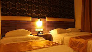 A hotel room with two beds, a nightstand with a lamp, and a patterned wall. - Clover Hotel (Masai)