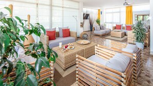 Un salón amplio con mobiliario de mimbre, una mesa de centro y plantas en macetas.