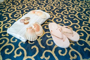A bed with a patterned blue and gold bedspread, a white towel with seashells, and pink flip-flops. - Hotel Horizonte (San Michele al Tagliamento)