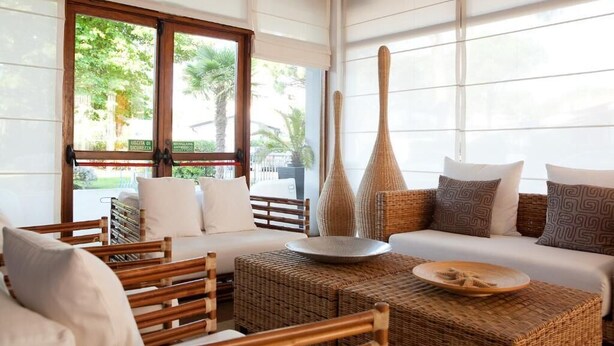 Una habitación con cama, muebles de mimbre y amplias ventanas con persianas.