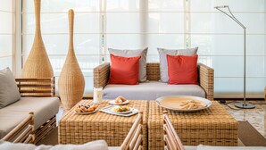 Una habitación acogedora con muebles de mimbre, un sofá con cojines rojo y gris, y una mesa de comedor con pasteles.