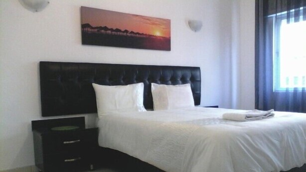 Ein Schlafzimmer mit einem großen Bett, einem Nachttisch, einem Wandbild und einem Fenster mit Vorhängen.