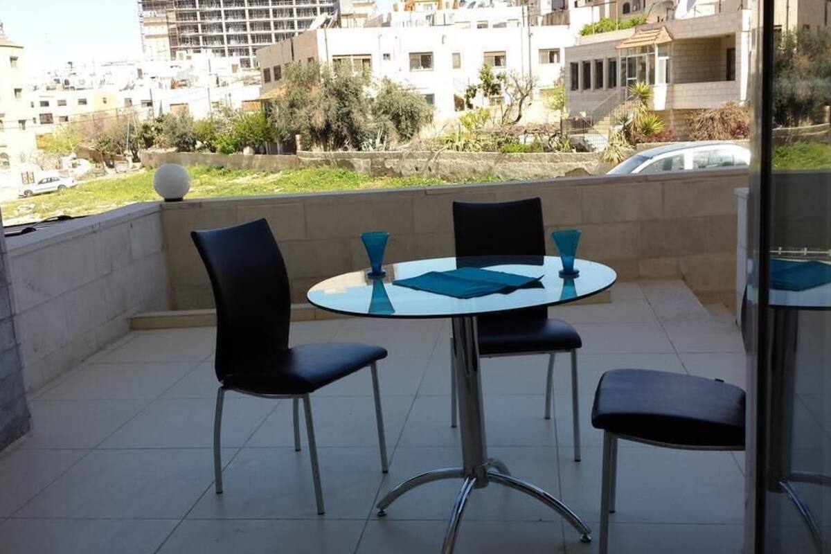 A balcony with a round table and four chairs, overlooking a residential area with buildings and greenery.