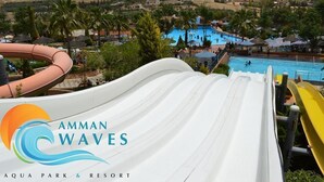 Ein Wasserpark mit einer großen weißen Rutsche, einem Poolbereich und Palmen.