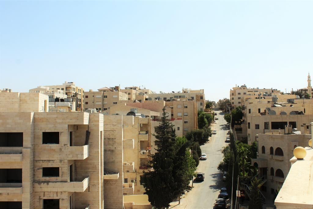 A street lined with multi-story buildings, some with balconies and satellite dishes.