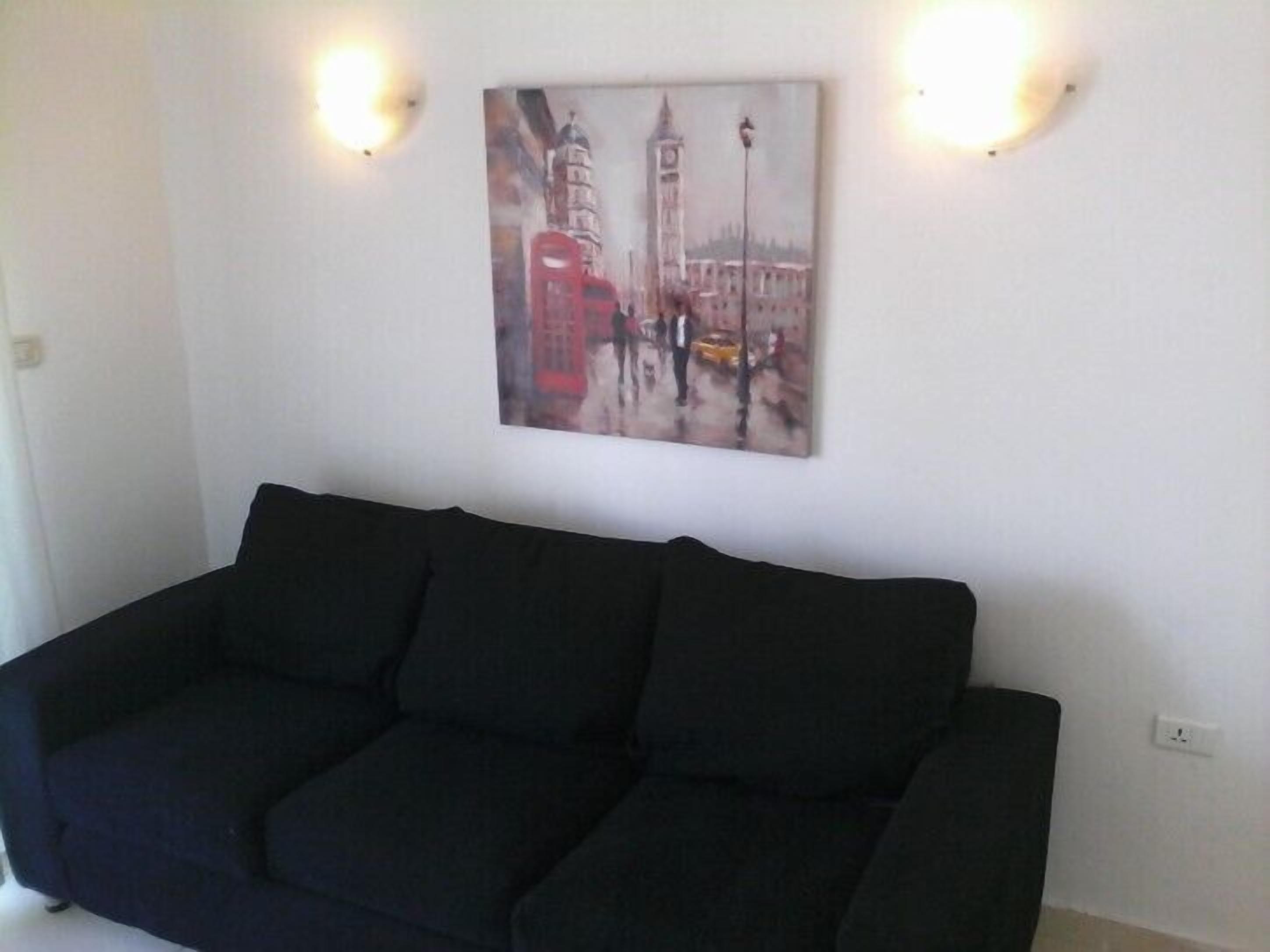 A living room with a black sofa, a painting of a cityscape, and two wall-mounted lights.