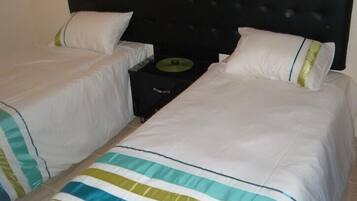 A double bed with white bedding and green stripes, a black headboard, and a bedside table with a green lamp.