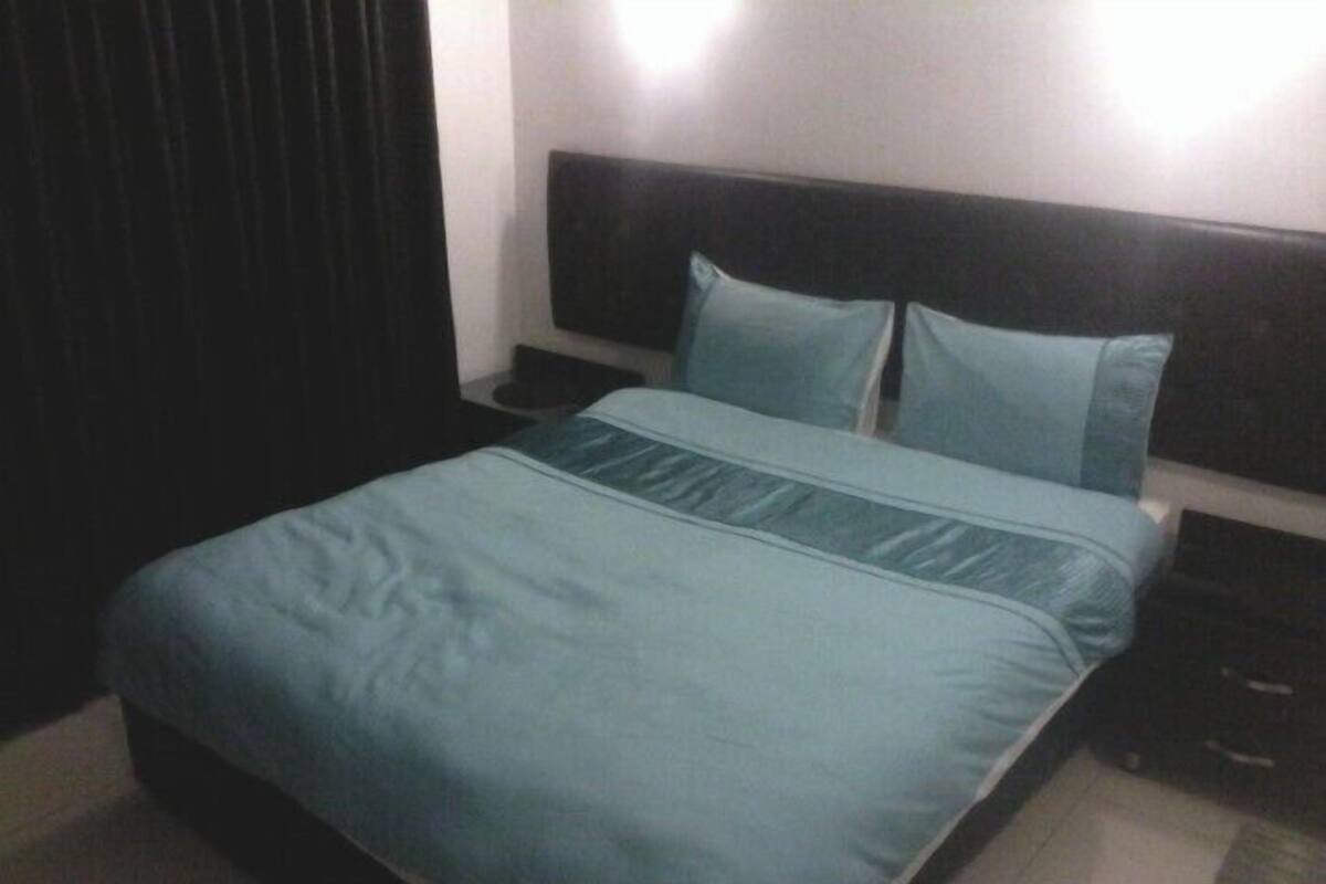 A neatly made bed with a blue bedspread and pillows, a dark headboard, and a nightstand with a lamp.
