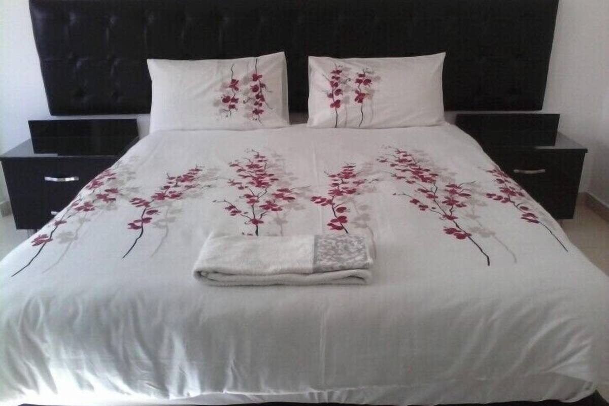 A bed with a white bedspread featuring red floral patterns, flanked by two white pillows with similar designs.
