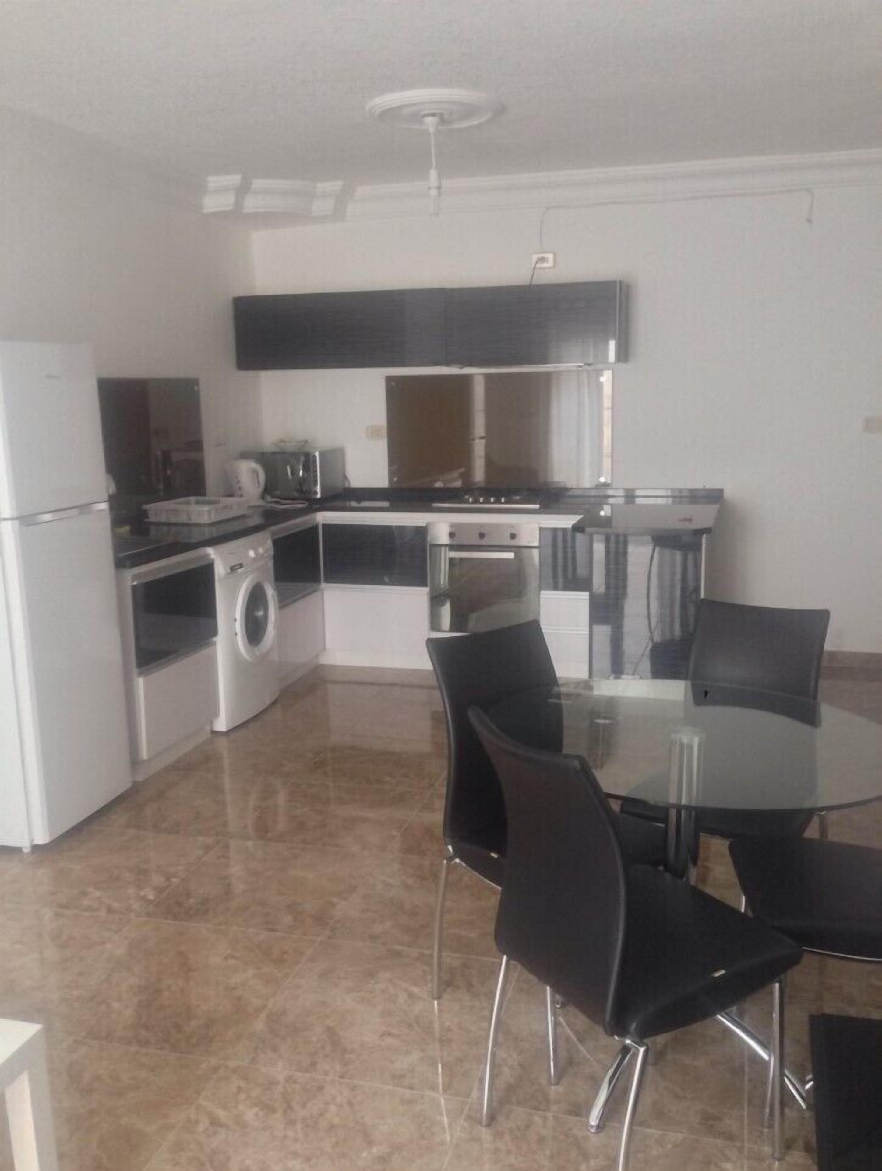 A compact kitchen with a stove, oven, and washing machine. There is a dining table with chairs and a ceiling light fixture.