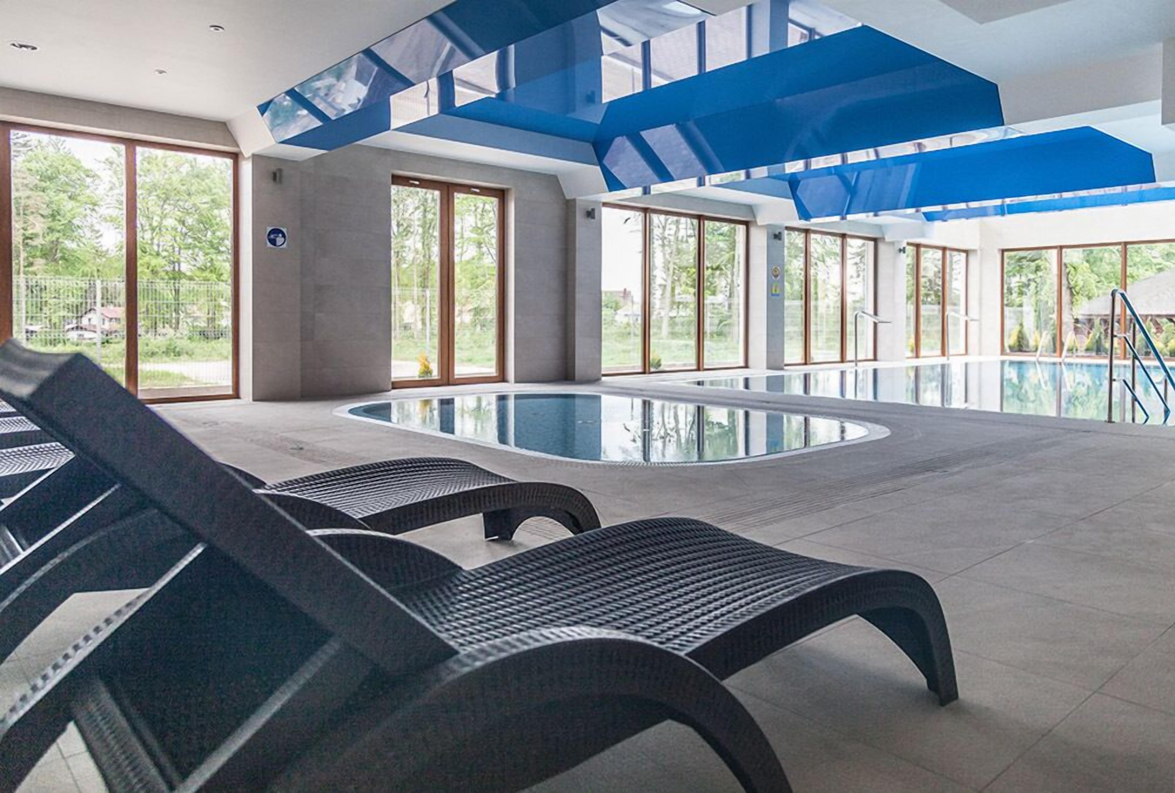 Une piscine intérieure moderne avec des parois en verre transparent, un espace central dédié à la baignade et des chaises longues.