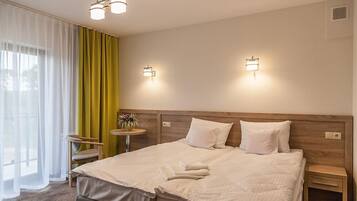 Ein Hotelzimmer mit einem großen Bett, zwei Nachttischen, einem kleinen runden Tisch mit Pflanze und einem Sessel.