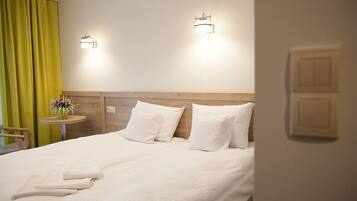 A hotel room with a large bed, two wall-mounted lights, a small table with a vase of flowers, and a green curtain.