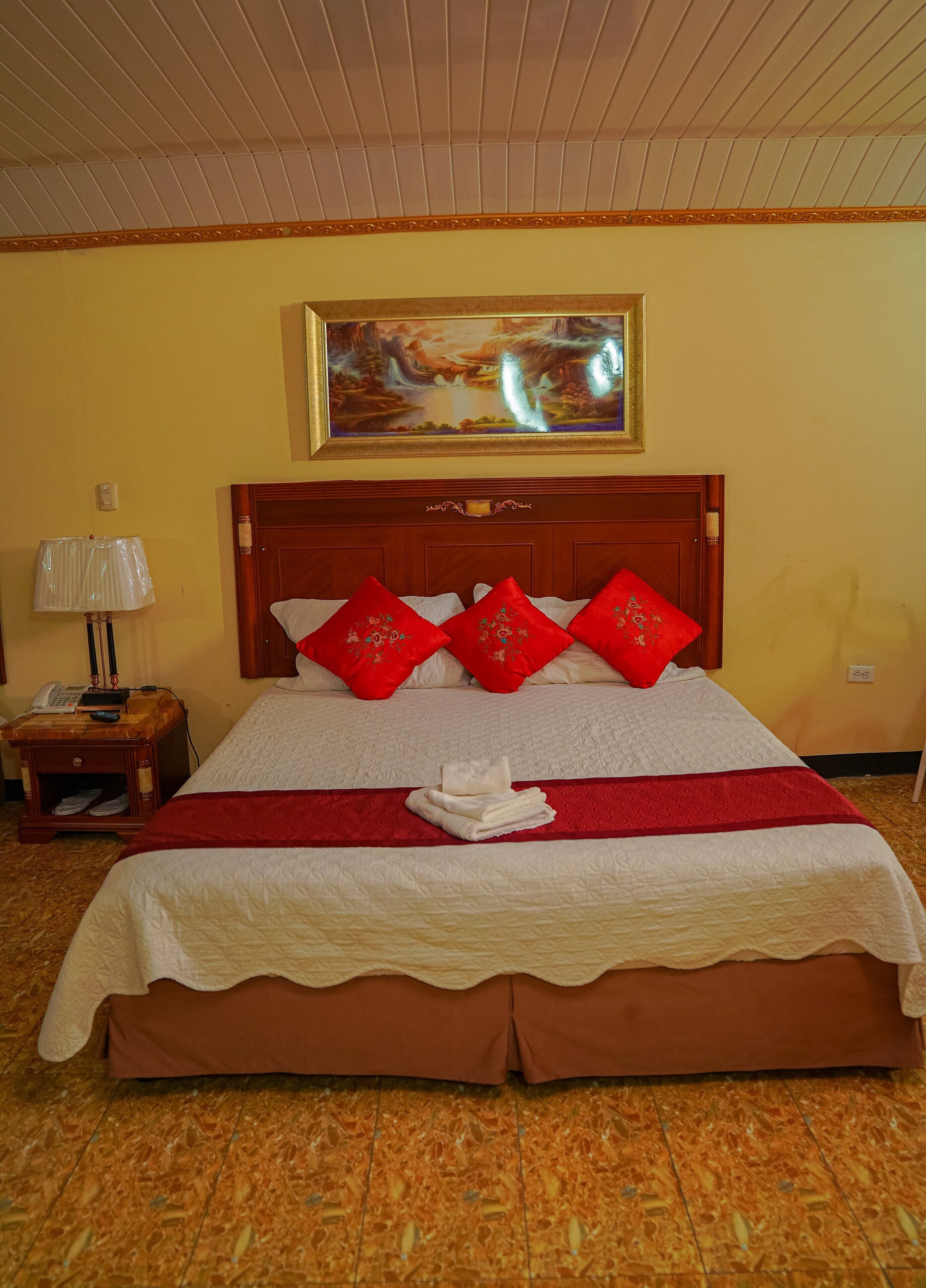 Une chambre d’hôtel avec un grand lit, des oreillers rouges et blancs, un tableau au mur, une table de chevet avec une lampe et une couvre-lit rouge et blanche.