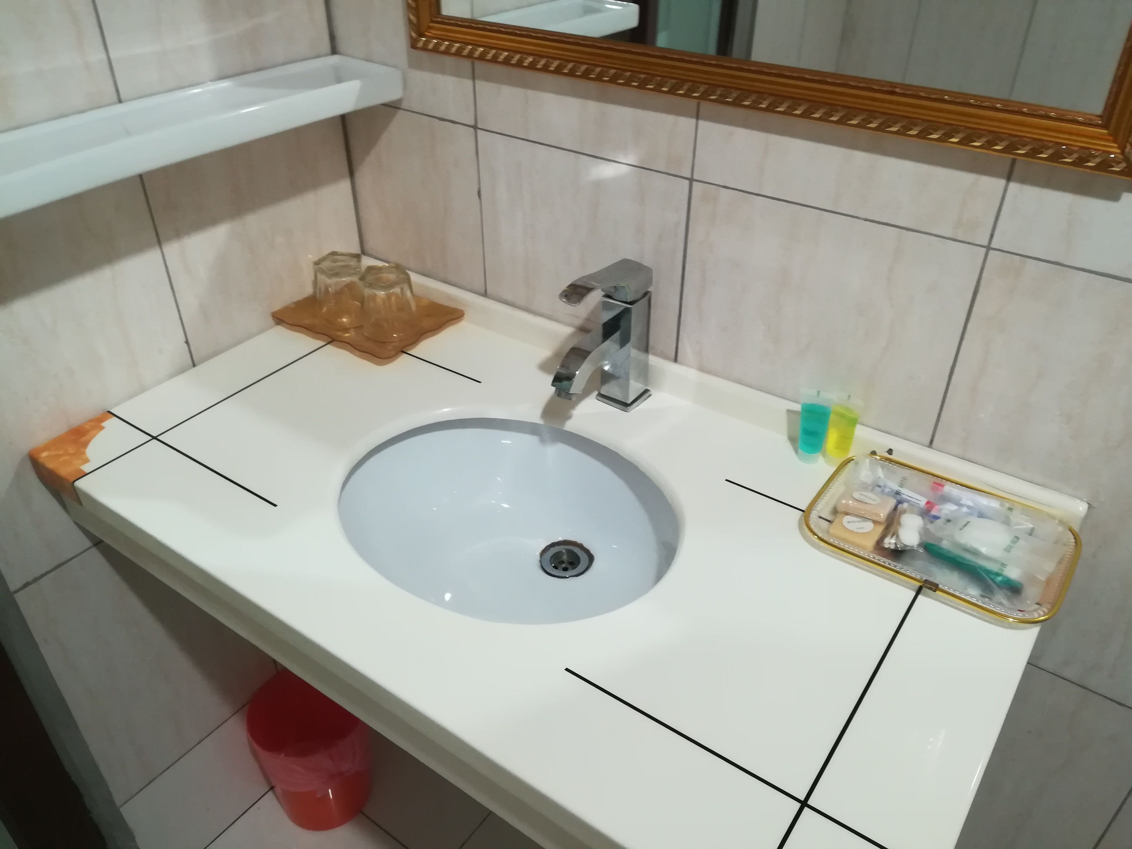 A bathroom sink with a mirror above it, a soap dispenser, and a trash bin.