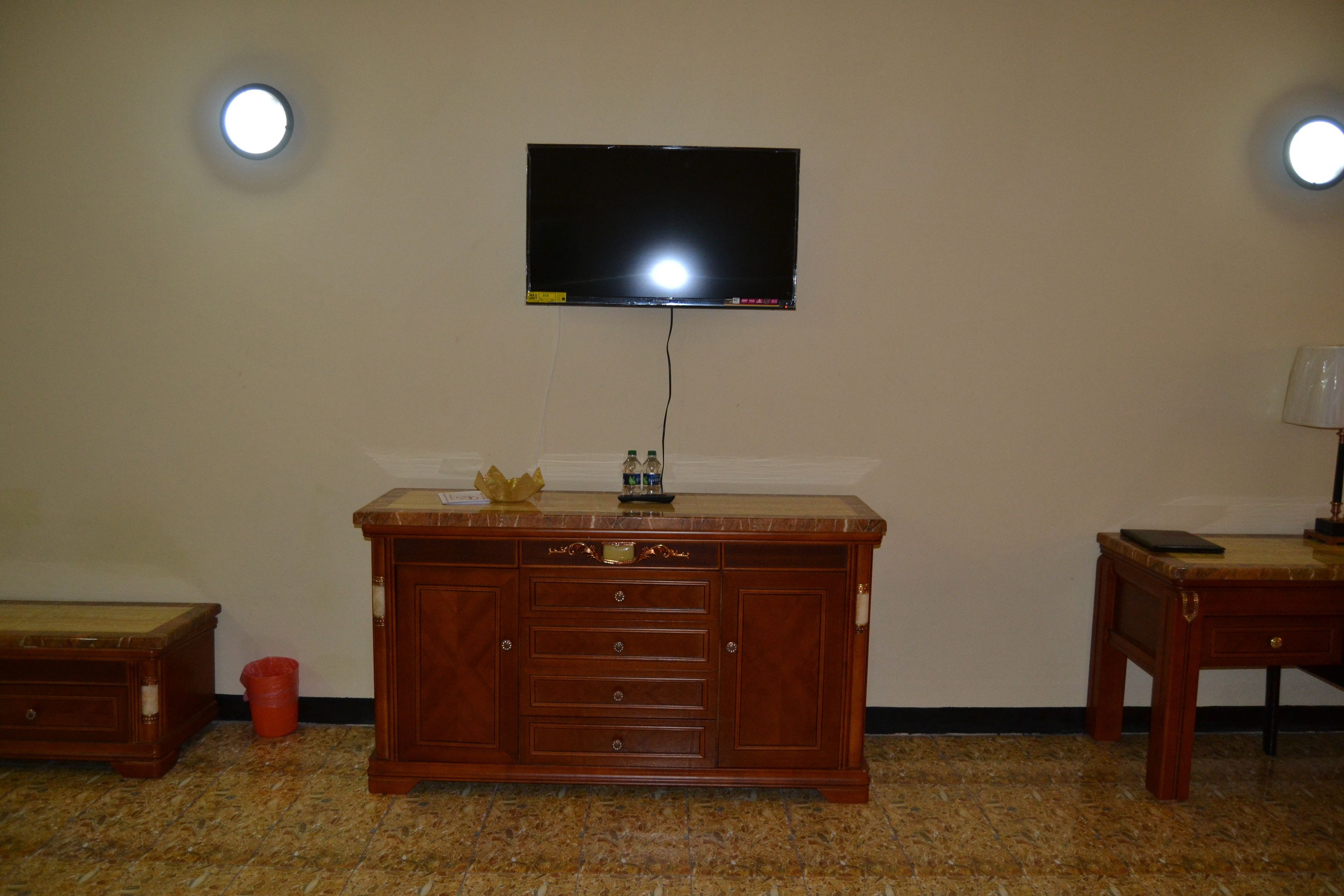 A room with a wooden cabinet, a television mounted on the wall, and a small table with a lamp.