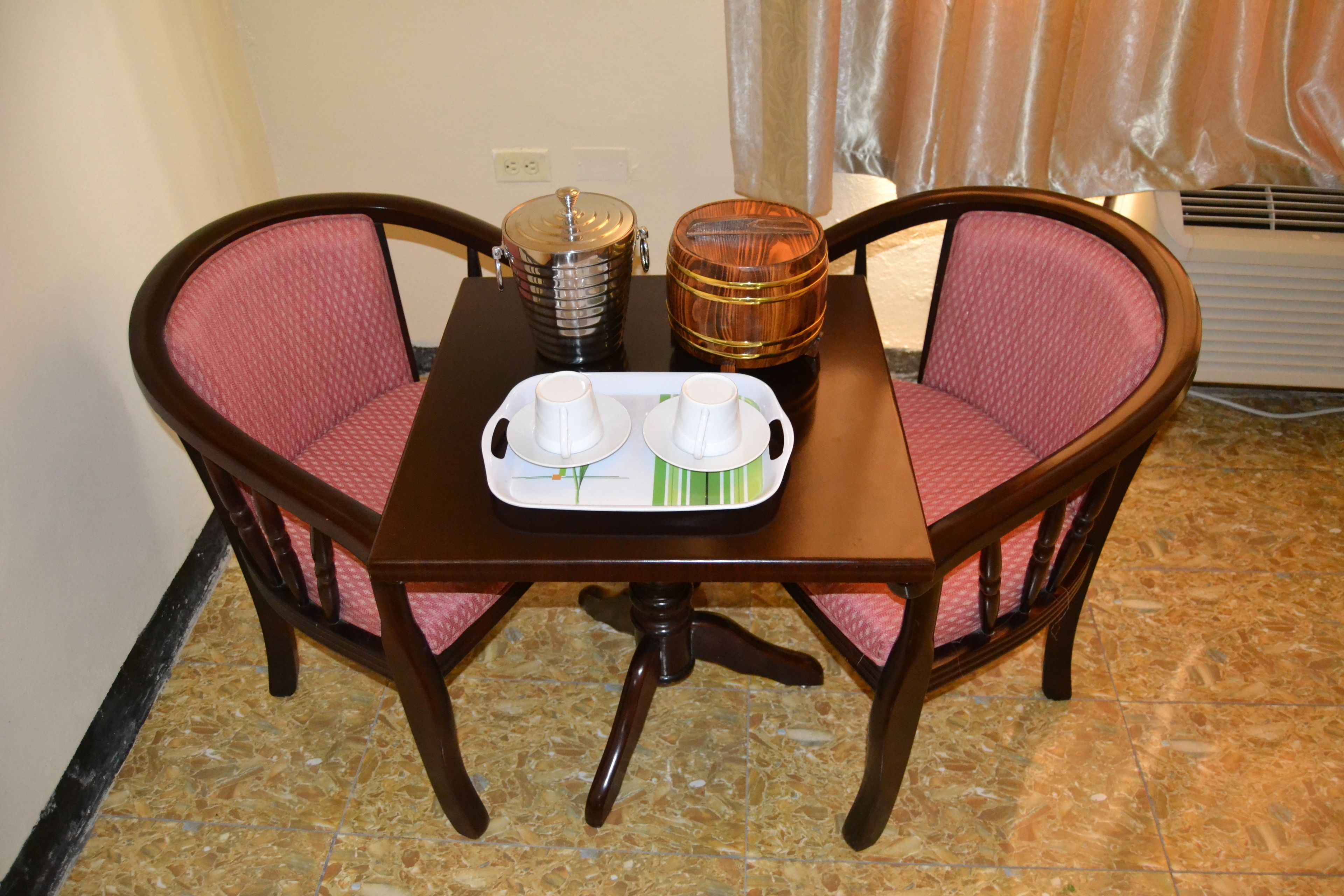 A dining table with two chairs, a tray with cups and saucers, and a coffee pot on the table.