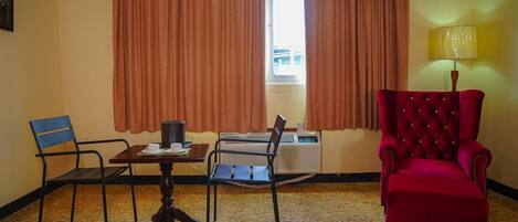 A room with a dining table, two chairs, a red armchair, a lamp, and a window with curtains.