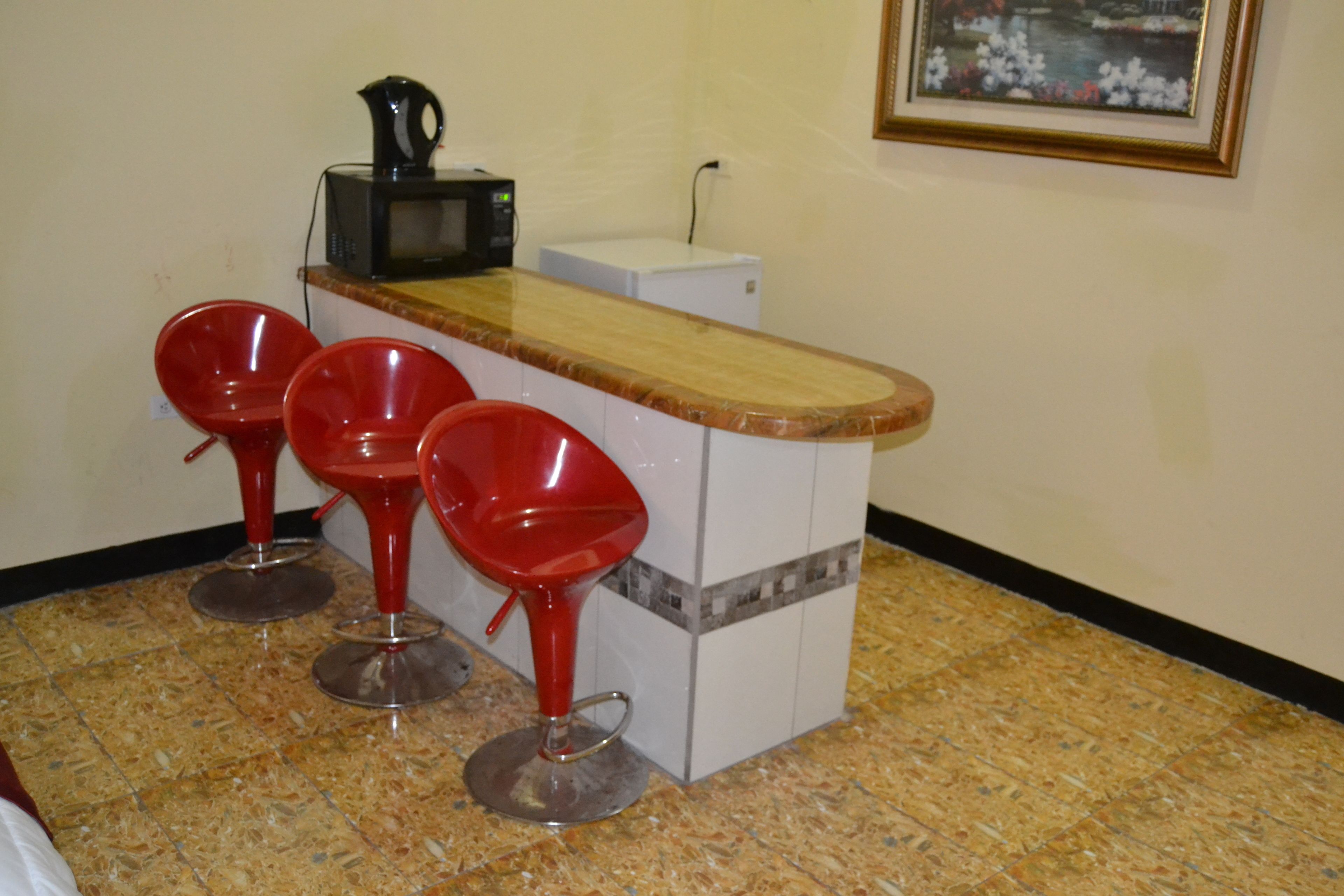 Cozinha com bancada de madeira, três banquetas vermelhas, uma cafeteira e uma geladeira branca.