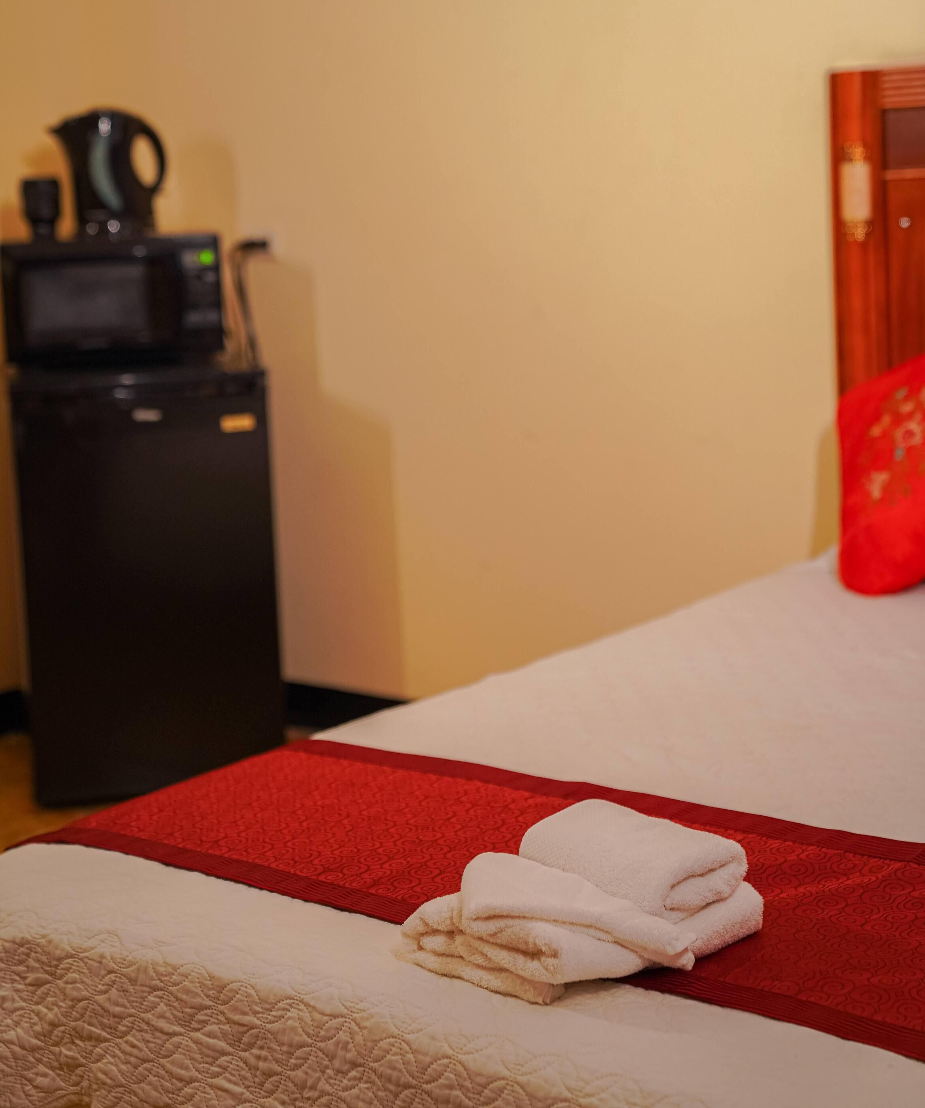 Ein Hotelzimmer mit einem Bett, einer roten Decke, einem weißen Handtuch und einer Kaffeemaschine.