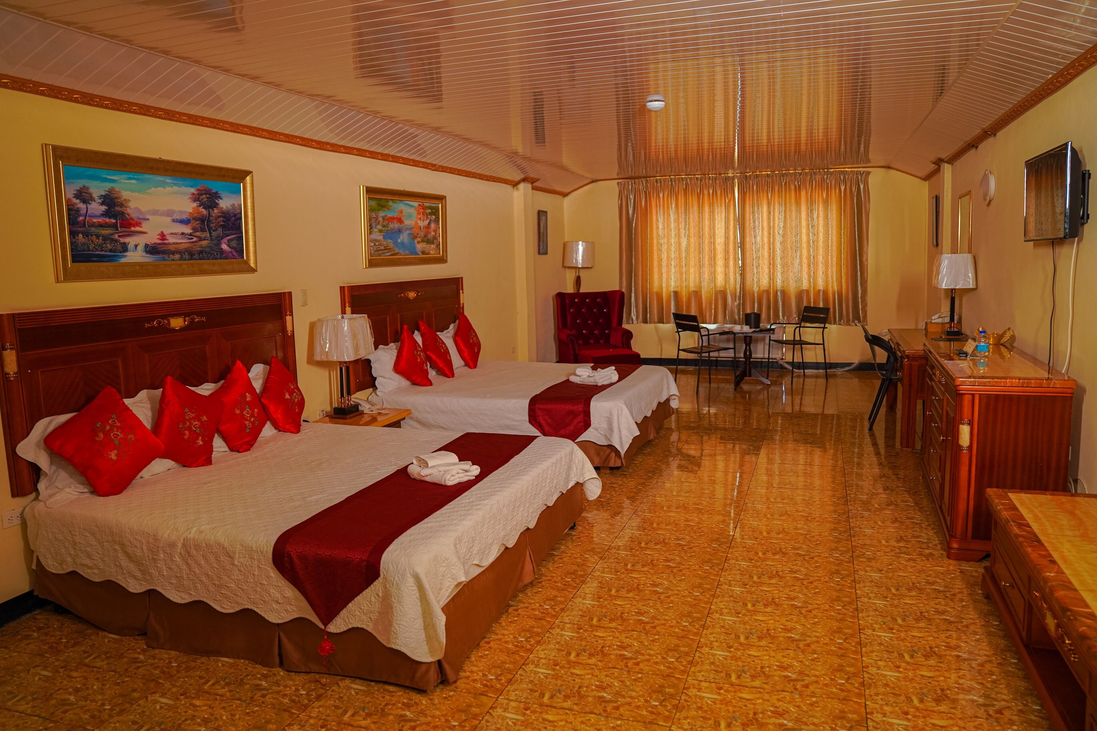 Habitación de hotel con dos camas, un escritorio, una silla, un televisor y obras de arte en las paredes.