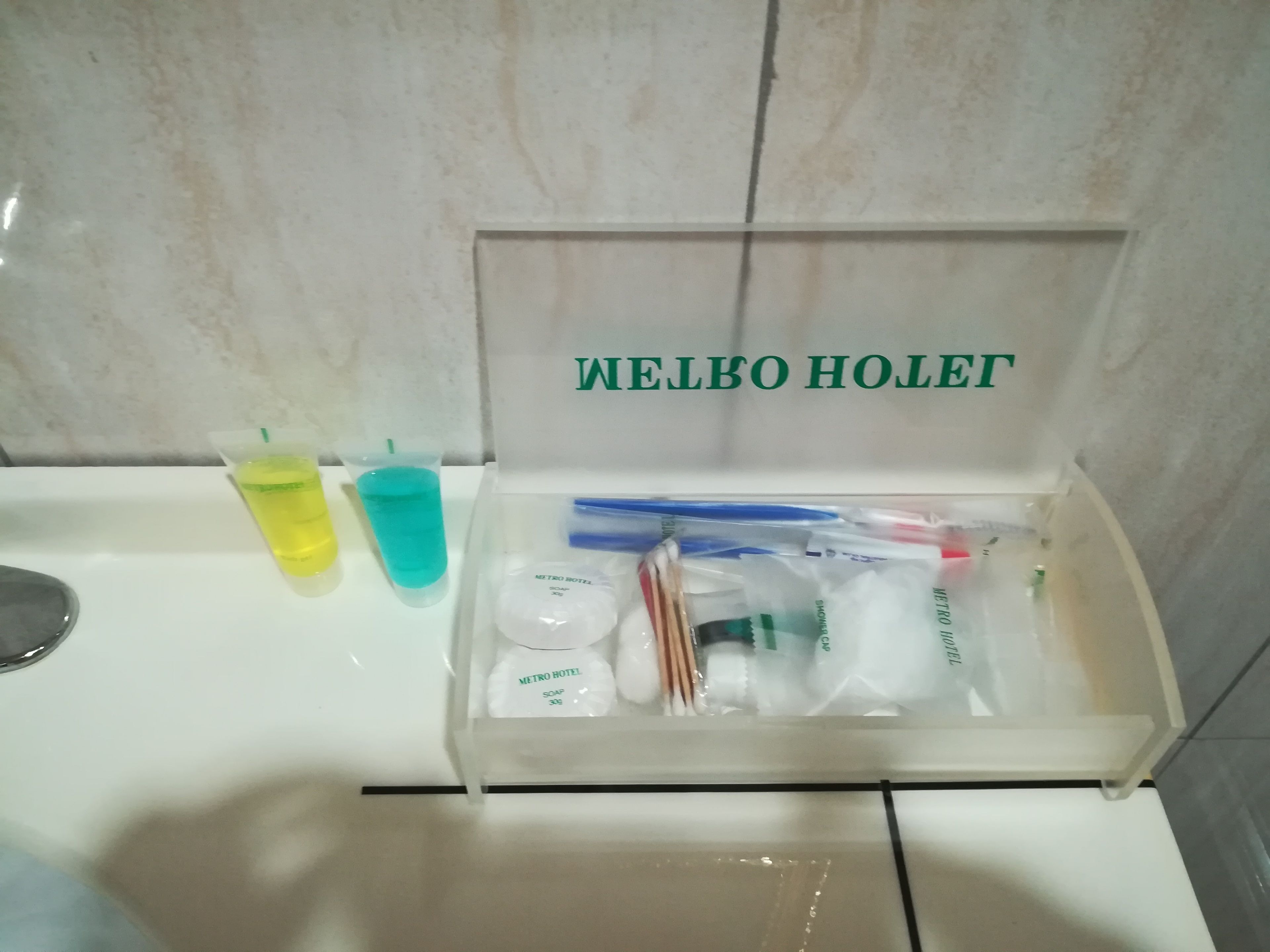 Een badkamer met een witte wastafel, een spiegel en toiletartikelen in een transparante doos met de tekst 'WELBO HOLET'.