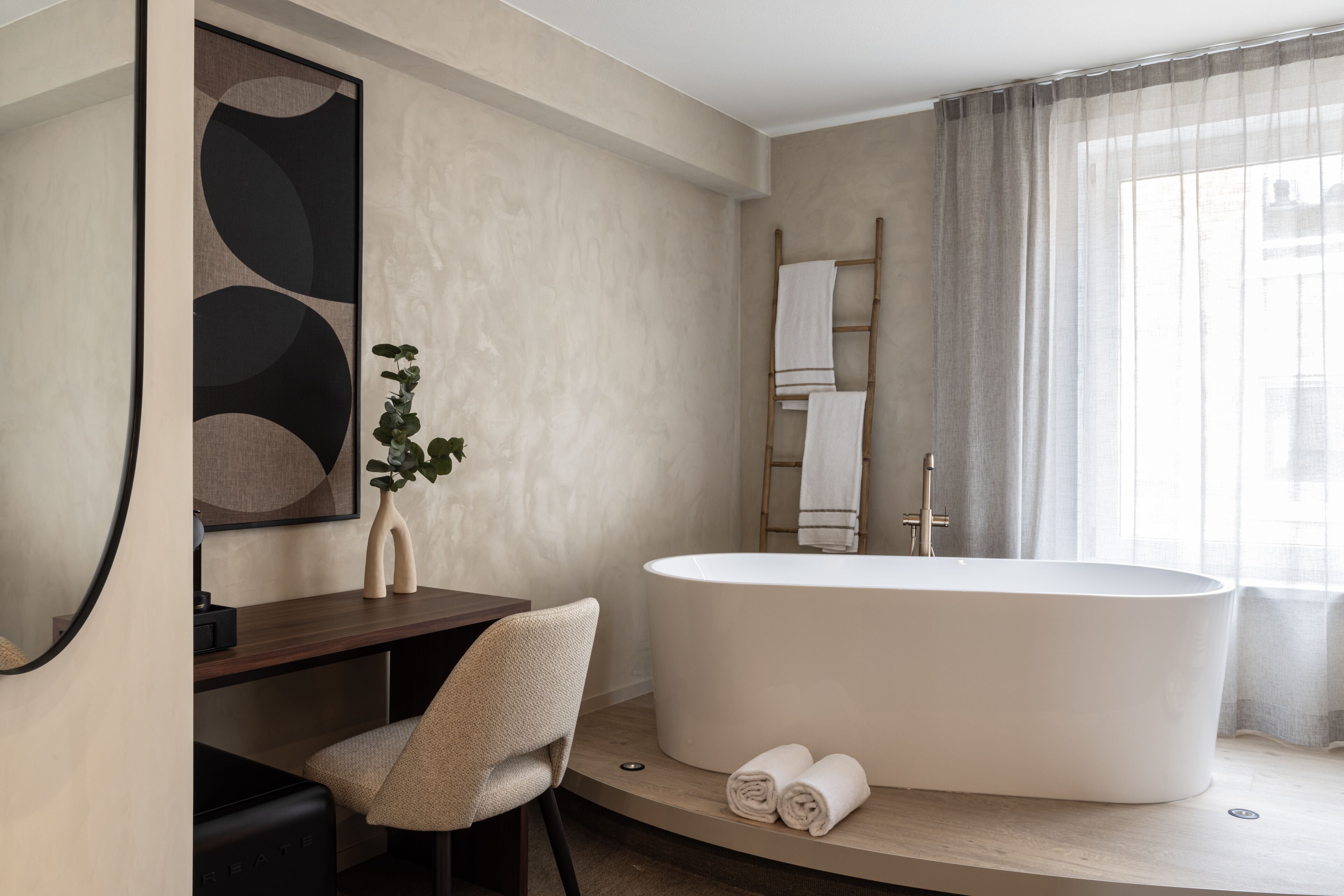 A modern bathroom with a freestanding bathtub, a wooden vanity, a chair, and a large mirror.