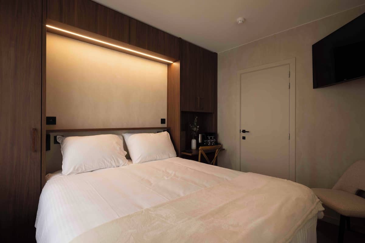 Una cama bien hecha con cabecera, una mesita de noche con lámpara y una silla.