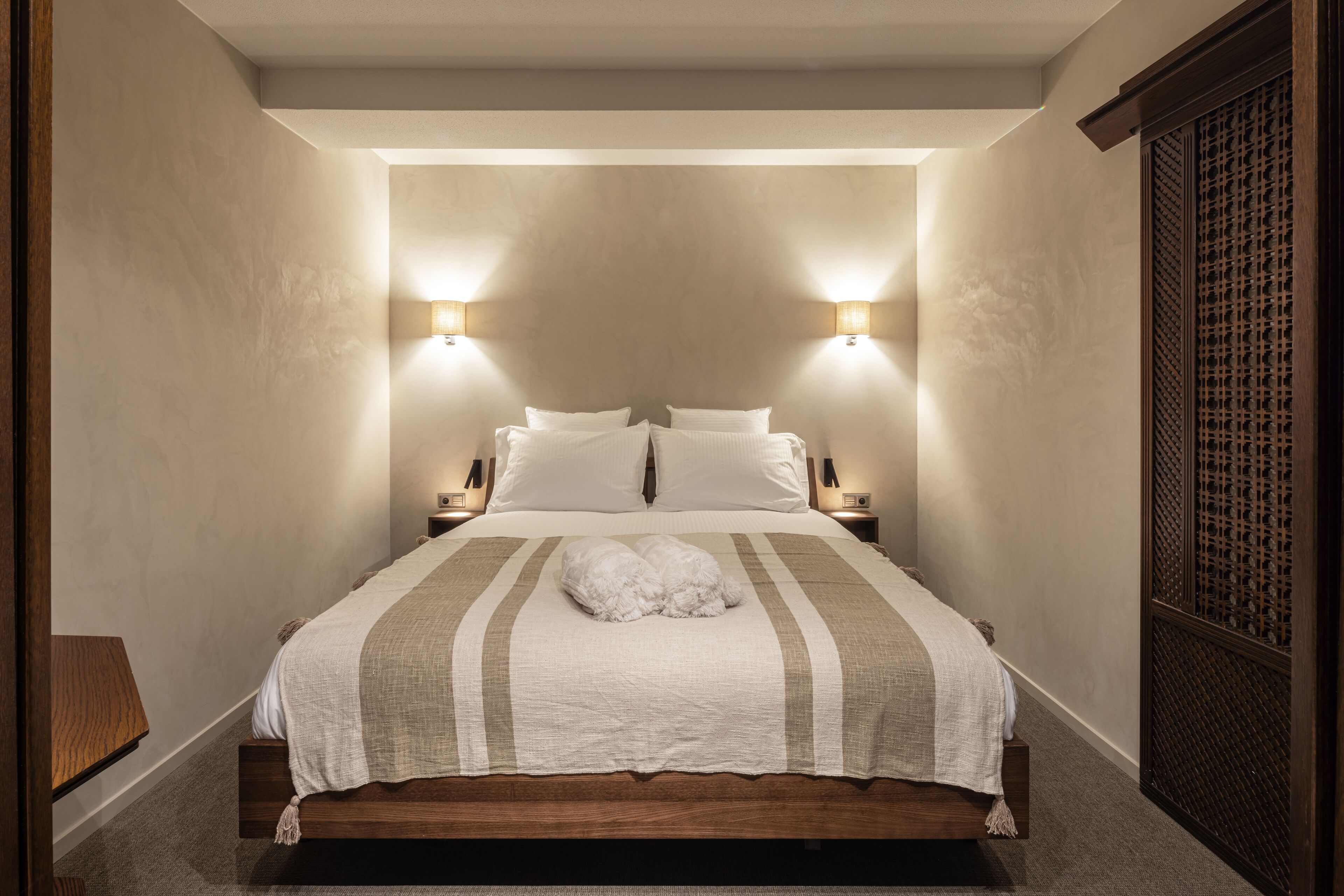 A neatly made bed with a striped bedspread and two wall-mounted lamps on either side.